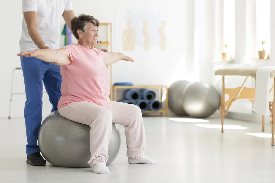Physiotherapist guiding a balance and mobility exercise on a stability ball